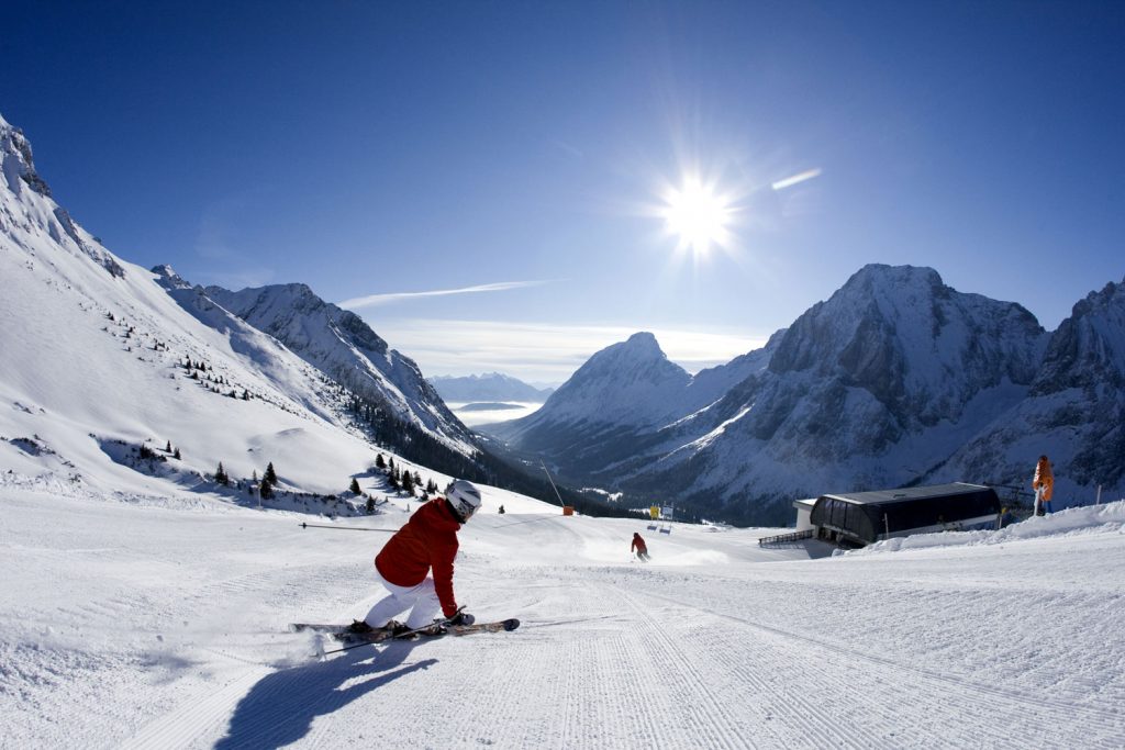 Skifahren auf verschneiten Pisten. Mit Skiern der Sonne entgegen, Berge im Hintergrund